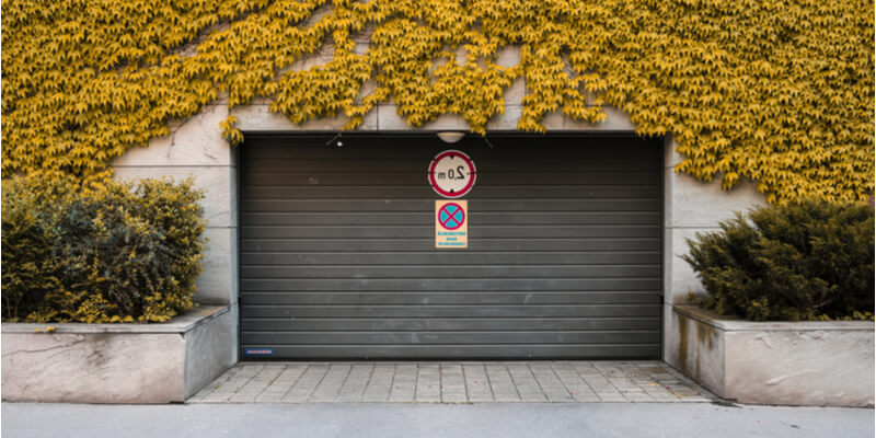 Modern black roller door set into a stone wall under autumn ivy